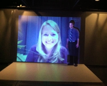 Riverstone Energy Center team members Kristy Johnson (on screen) and Ben Thompson (standing) make first trial run using the modeling and simulation “Cave” for immersive teleconferencing.